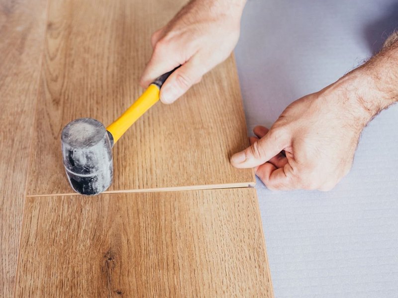 person hammering hardwood plank