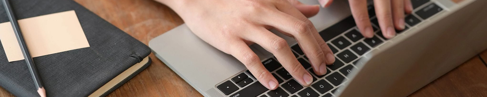 person typing at laptop with notebook next to them